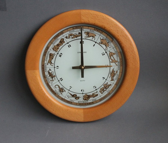 Image 1 of Horloge murale vintage Junghans avec boîtier en bois et signe du zodiaque sur un cadran en verre.