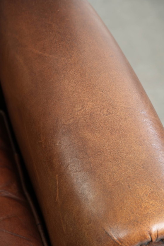 Image 1 of Precioso sillón orejero de piel de oveja marrón oscuro con un aspecto atemporal en un tamaño sutil.