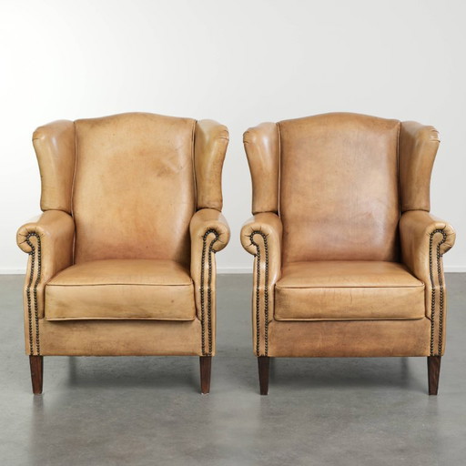 Dos hermosos sillones orejeros de piel de vaca clara con un estilo inglés atemporal y gran comodidad.