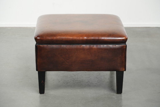 Image 1 of Grote donkerbruine vierkante hocker gemaakt van schapenleer met zwarte biezen