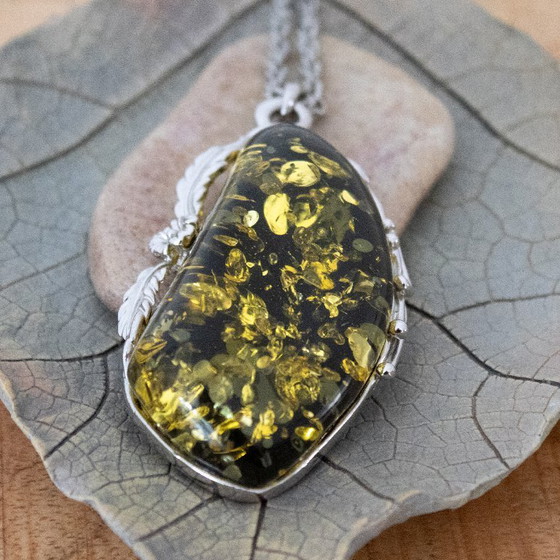 Image 1 of Grande ciondolo in ambra baltica verde: incastonato in metallo color argento con decorazioni floreali.