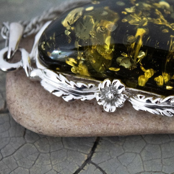 Image 1 of Grande ciondolo in ambra baltica verde: incastonato in metallo color argento con decorazioni floreali.