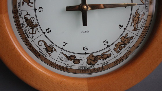 Image 1 of Horloge murale vintage Junghans avec boîtier en bois et signe du zodiaque sur un cadran en verre.