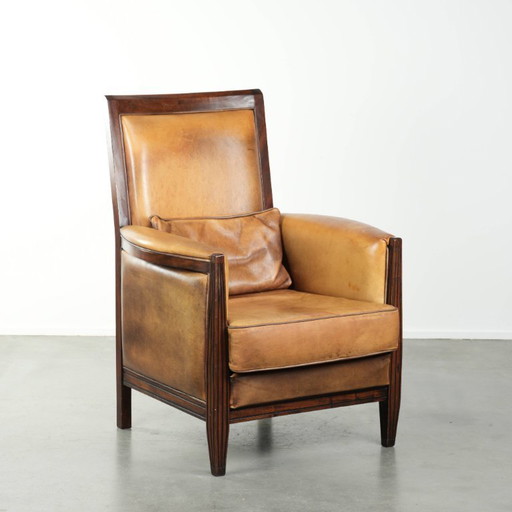 Cómodo sillón de diseño Art Déco en color coñac, fabricado en piel de oveja combinada con madera y con respaldo alto.