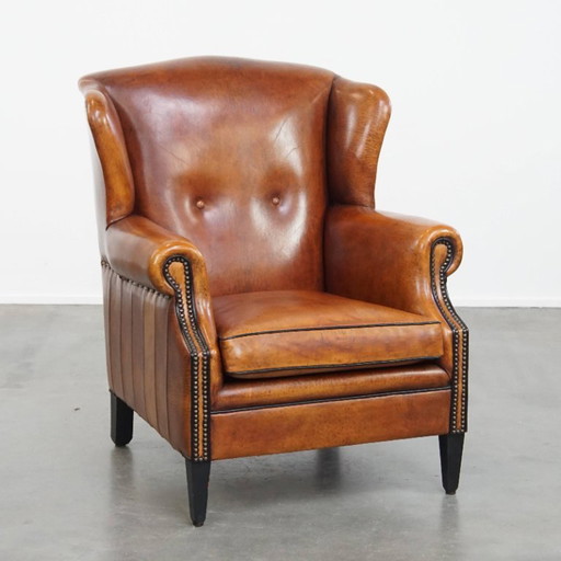 Comfortabele schapenleren oorfauteuil met een prachtige warme kleurstelling en een afwerking met stiksels en zwarte biezen