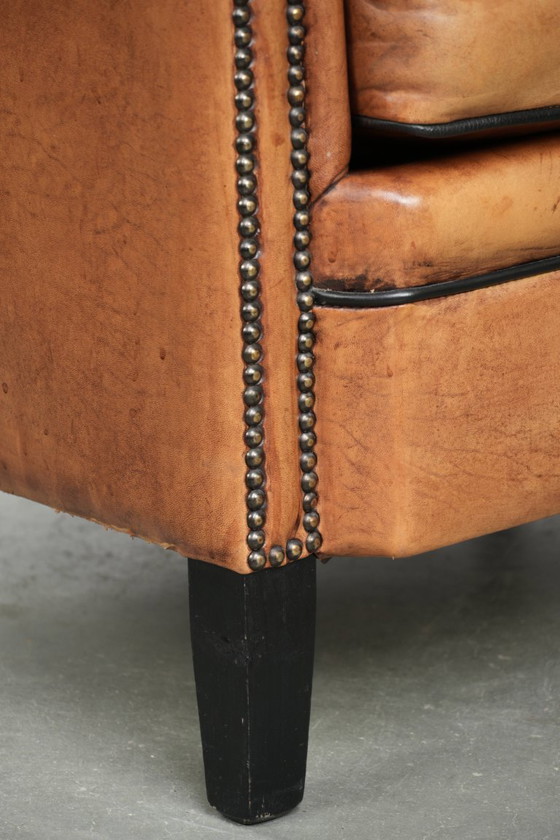 Image 1 of Amplio sillón club de estilo inglés, tapizado en piel de oveja, con acabado de clavos decorativos y ribetes negros.