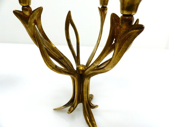 Image 1 of Een paar messing kandelaars met drie lichtpunten op een statief, versierd met organische bloemmotieven, circa 1960-1970.