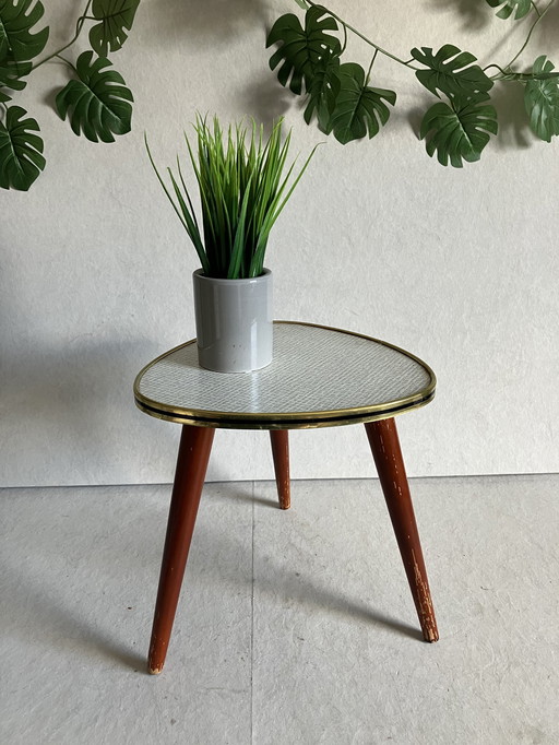 A Nice Vintage Plant Table From The 50s And 60s With Formica Top. Around the top is a strip in brass and black color.