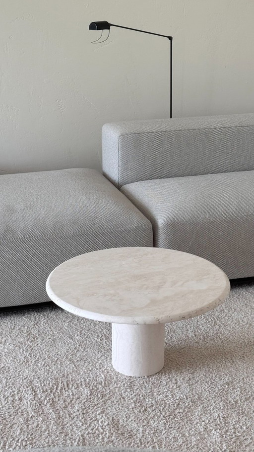 Round coffee table made of light-colored natural stone with a cylindrical base in a minimalist design.
