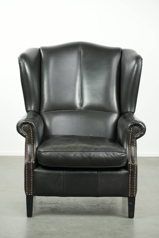 Zwarte rundleren oorfauteuil in een klassiek Engelse stijl