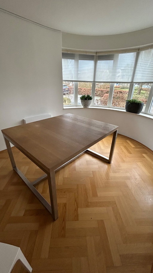Mesa de comedor de diseño con estructura de acero inoxidable y marco de roble blanqueado.