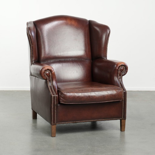 Elegante poltrona vintage con schienale alto in pelle di pecora, dal look inglese senza tempo, rifinita con borchie decorative.