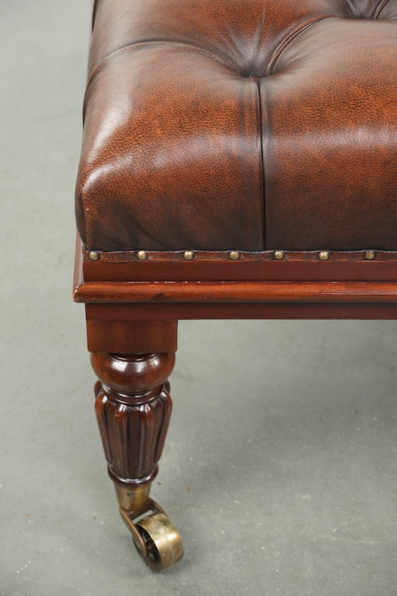 Image 1 of Grote bruine rundleren chesterfield hocker in Engelse stijl met sierlijke poten en messing wieltjes