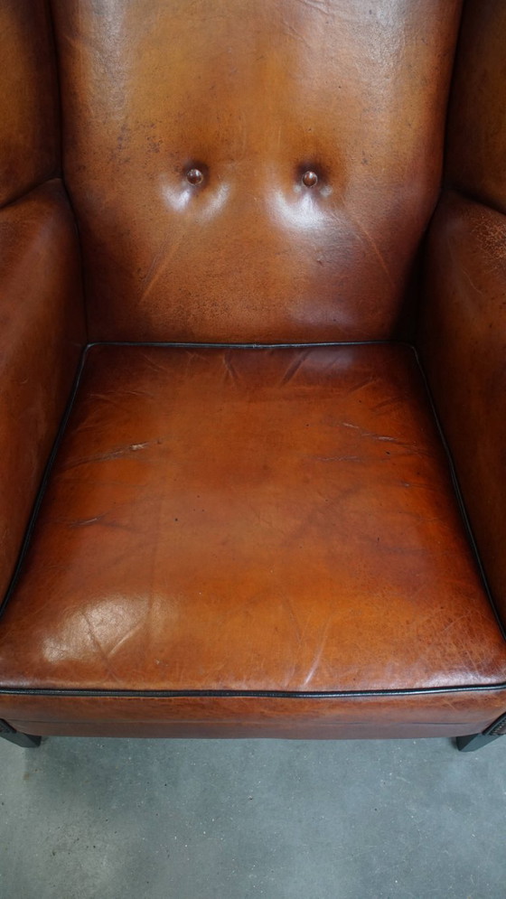 Image 1 of Schapenleren oorfauteuil met een warme kleurstelling en een afwerking met siernagels en zwarte biezen