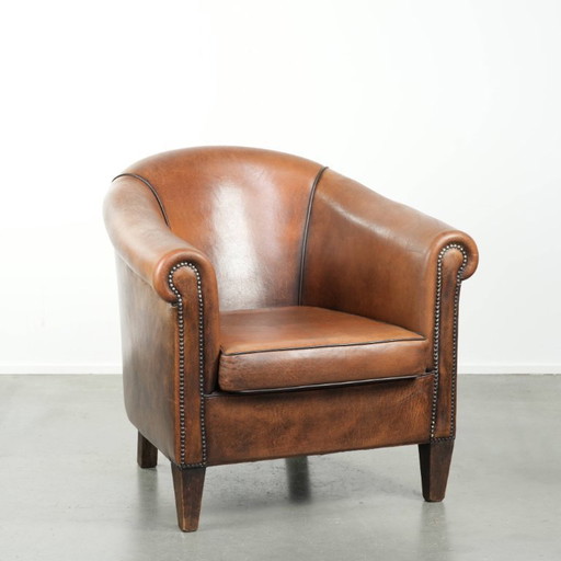 Schapenleren clubfauteuil met een mooie patina en een verfijnde afwerking met zwarte biezen