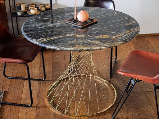 Lujosa mesa de comedor redonda con tablero de mármol negro y base dorada.