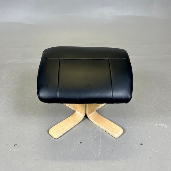 Image 1 of Two‑piece lounge set by Ekornes comprising a swivel reclining armchair and a matching footstool in black leather with a wood fra
