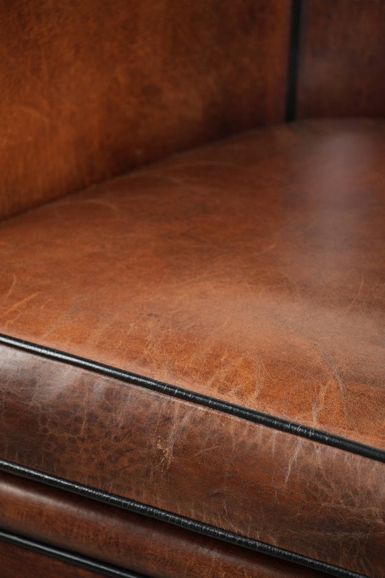 Image 1 of Mooie en karaktervolle schapenleren clubfauteuil met mooie diepe warme kleuren, zwarte biezen en een comfortabele zit