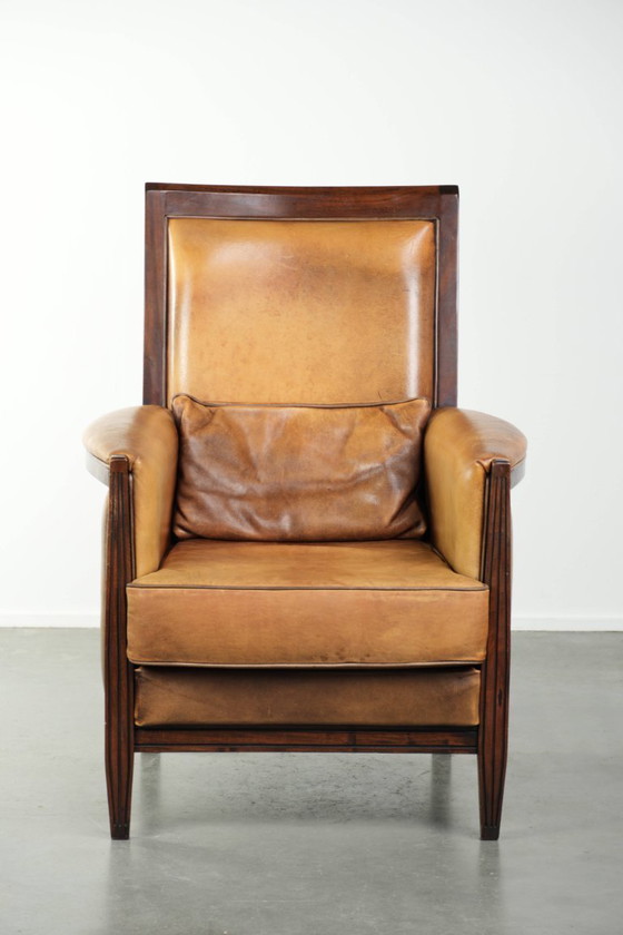 Image 1 of Cómodo sillón de diseño Art Déco en color coñac, fabricado en piel de oveja combinada con madera y con respaldo alto.