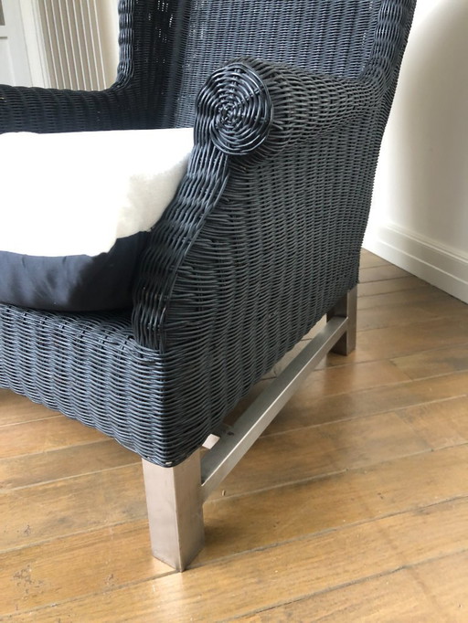 Fauteuil relaxant en osier noir et piètement en acier inoxydable.