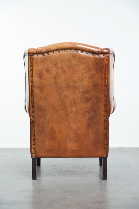 Image 1 of Grote oorfauteuil gemaakt van schapenleer met zwarte biezen en siernagels