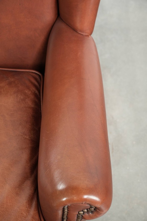Image 1 of Comoda poltrona a orecchioni in pelle bovina color cognac in stile inglese.
