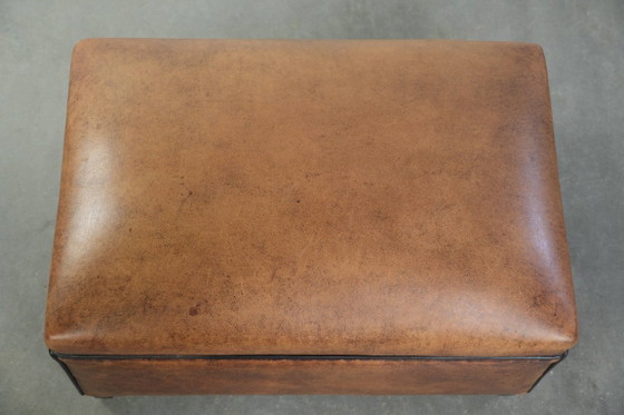 Image 1 of Characterful sheepskin footstool/ottoman with a beautiful patina and finished with black piping.