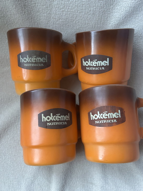 Image 1 of Dit is een set vintage Hotcemel Nutricia kopjes of mokken van oranje opaalglas met een kleurverloop.