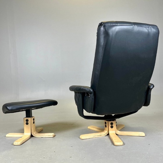 Image 1 of Two‑piece lounge set by Ekornes comprising a swivel reclining armchair and a matching footstool in black leather with a wood fra