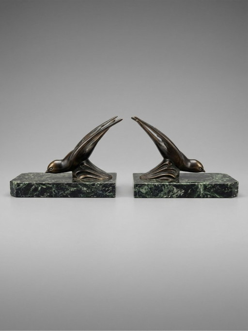 Een paar art-deco boekensteunen – zwaluwen van gepatineerd zink op groene marmeren voetstukken.