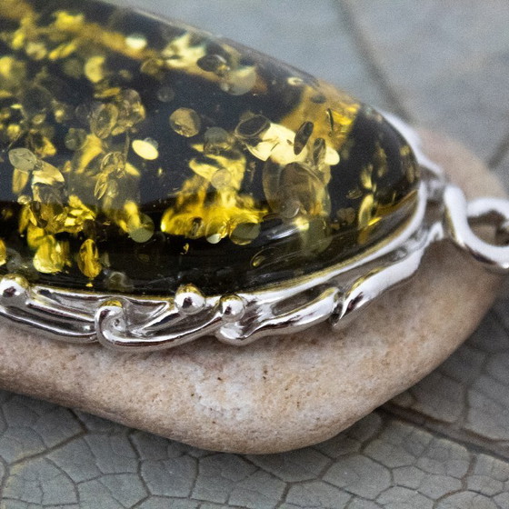 Image 1 of Grande ciondolo in ambra baltica verde: incastonato in metallo color argento con decorazioni floreali.