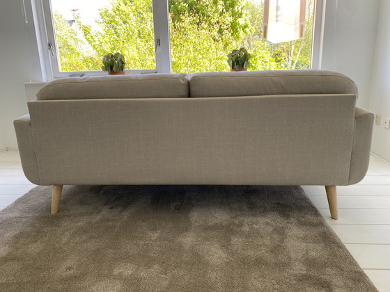 Image 1 of Elegante sofá de 3 plazas con tapicería de tela beige y patas de madera.