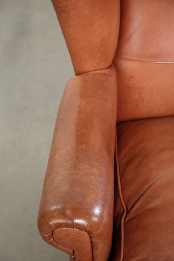 Image 1 of Fauteuil à oreilles en cuir de vachette couleur cognac clair, avec passepoil assorti et un style anglais plein de caractère.