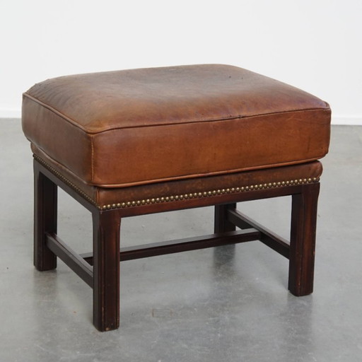 Hocker en cuir de mouton avec un cadre en bois et une finition avec des rivets décoratifs.