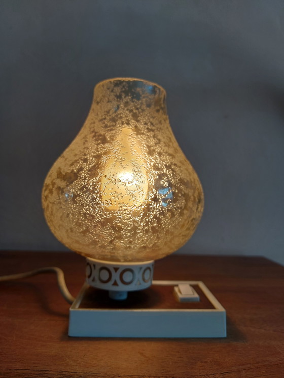 Image 1 of vintage tafellamp met een witte basis en een kap van gestructureerd, amber glas. 