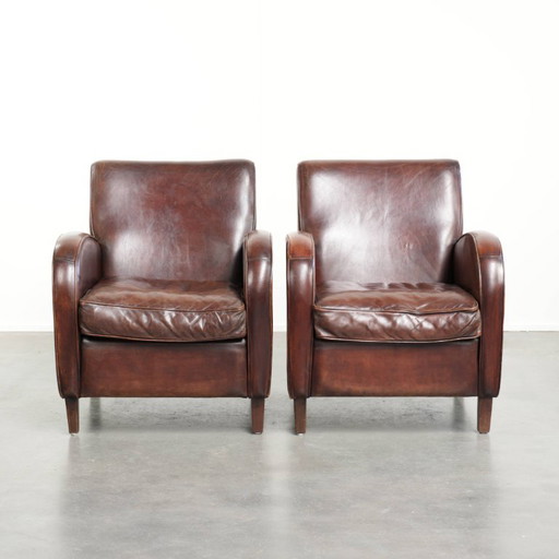 2x dunkel cognacfarbene Schaffellsessel mit abgerundeten Formen und elegantem Design