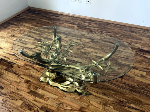 Sculpturale salontafel in de vorm van een boom, gemaakt van gegoten metaal, met een ovaal glazen blad.