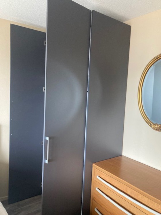 Image 1 of Hoher, dunkelgrauer zweitüriger Kleiderschrank mit vertikalen silbernen Griffen.