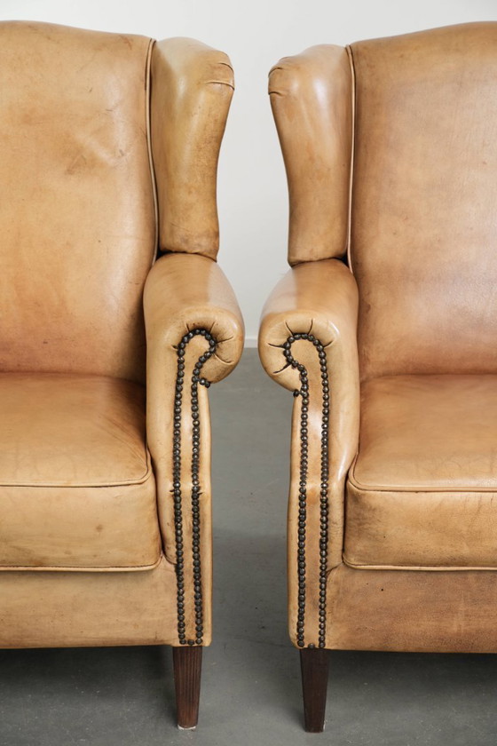 Image 1 of Dos hermosos sillones orejeros de piel de vaca clara con un estilo inglés atemporal y gran comodidad.