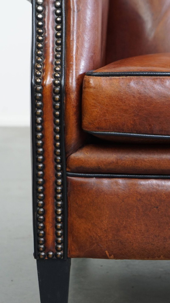 Image 1 of Schapenleren oorfauteuil met een warme kleurstelling en een afwerking met siernagels en zwarte biezen