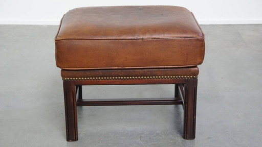 Hocker en cuir de mouton avec un cadre en bois et une finition avec des rivets décoratifs.