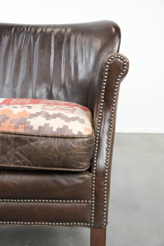 Image 1 of Subtiele donkerbruine fauteuil gemaakt van rundleer met een omkeerbaar Kelim zitkussen