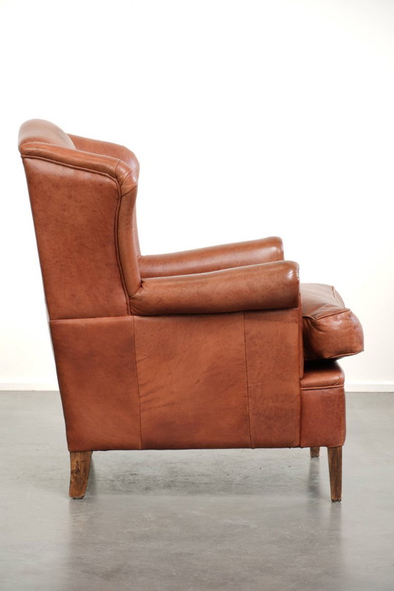 Image 1 of Fauteuil à oreilles en cuir de vachette couleur cognac clair, avec passepoil assorti et un style anglais plein de caractère.