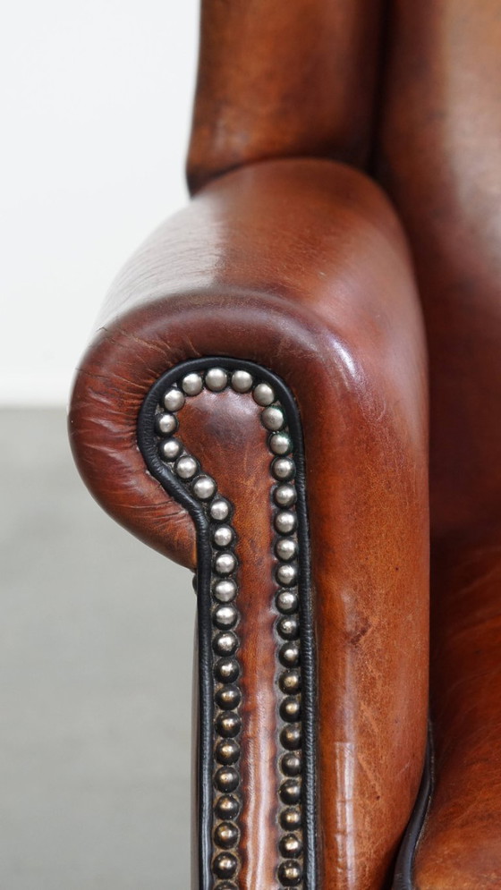 Image 1 of Schapenleren oorfauteuil met een warme kleurstelling en een afwerking met siernagels en zwarte biezen