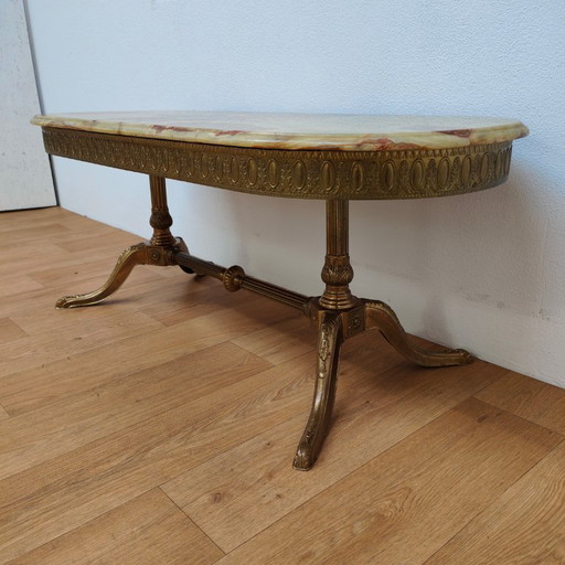 Table basse ovale de style Hollywood Regency avec plateau en marbre et piètement en laiton.
