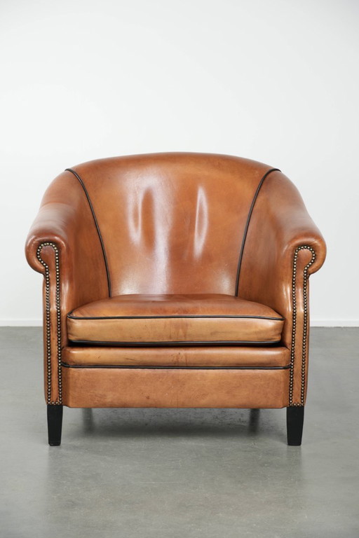 Amplio sillón club de estilo inglés, tapizado en piel de oveja, con acabado de clavos decorativos y ribetes negros.