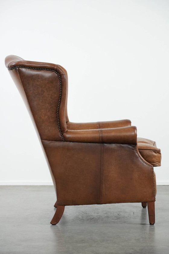 Image 1 of Tijdloze cognac kleurige oorfauteuil in Engelse stijl gemaakt van rundleer afgewerkt met siernagels
