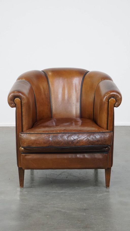 Fauteuil club vintage unique en cuir couleur cognac avec passepoil noir