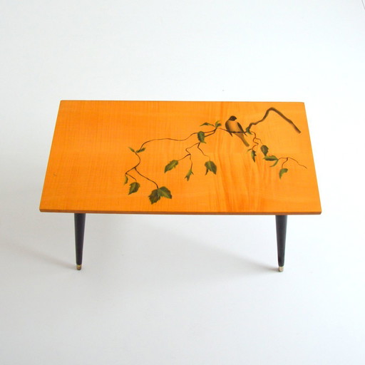 Pretty coffee table from the 50s/60s.  Decorated with a bird on a branch.  Black brass-finish tapered legs.  L 80/ W 40/ H 51