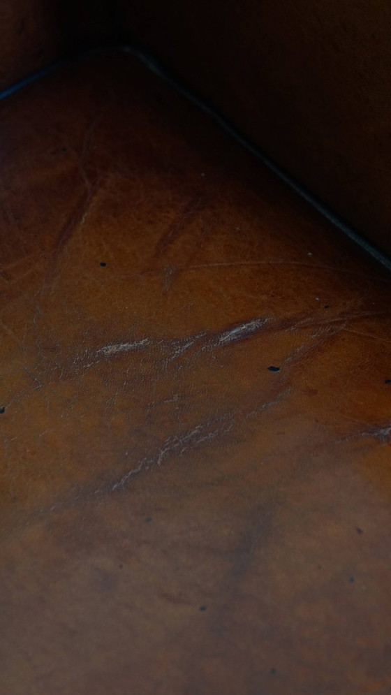 Image 1 of Schapenleren oorfauteuil met een warme kleurstelling en een afwerking met siernagels en zwarte biezen